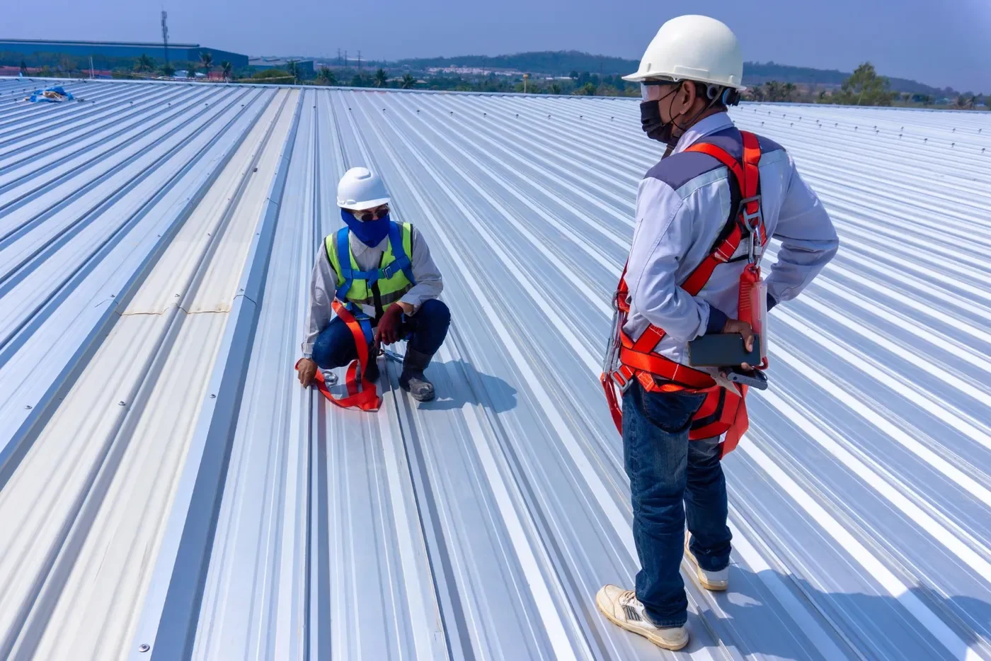Commercial roofing contractors with safety harnesses inspecting metal panel roof on industrial building in Pleasanton roofing California